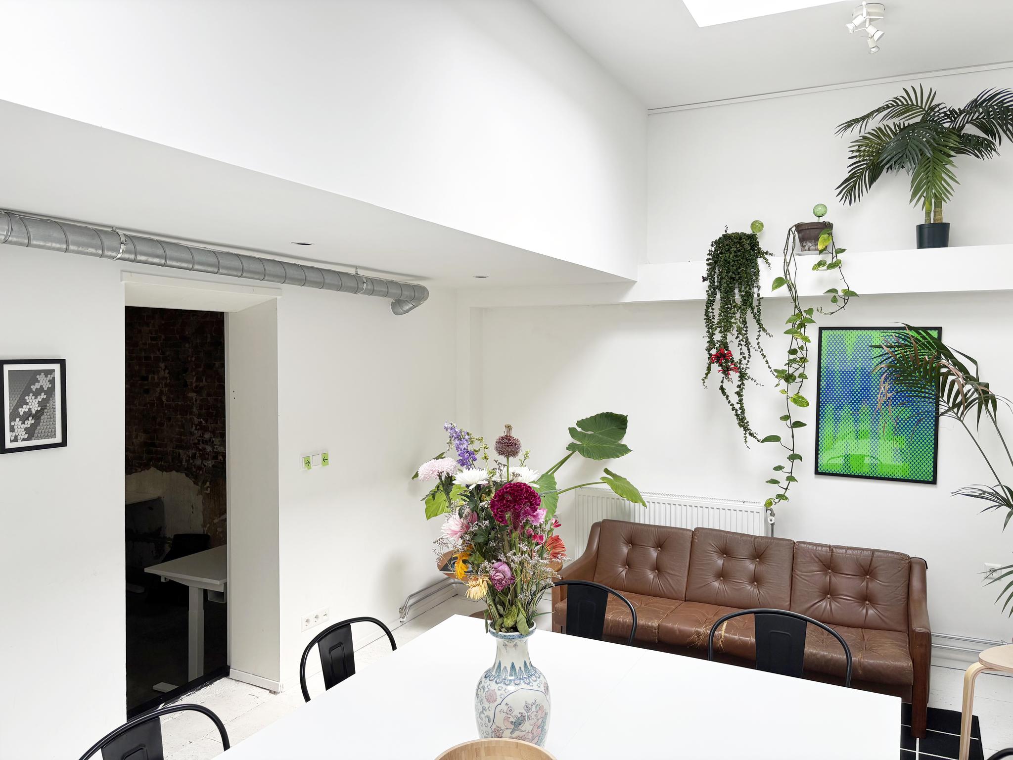 Moderne, lichte ruimte aan de Van Ostadestraat met een witte eettafel, bruine leren bank, planten en kleurrijke kunst aan de muur.